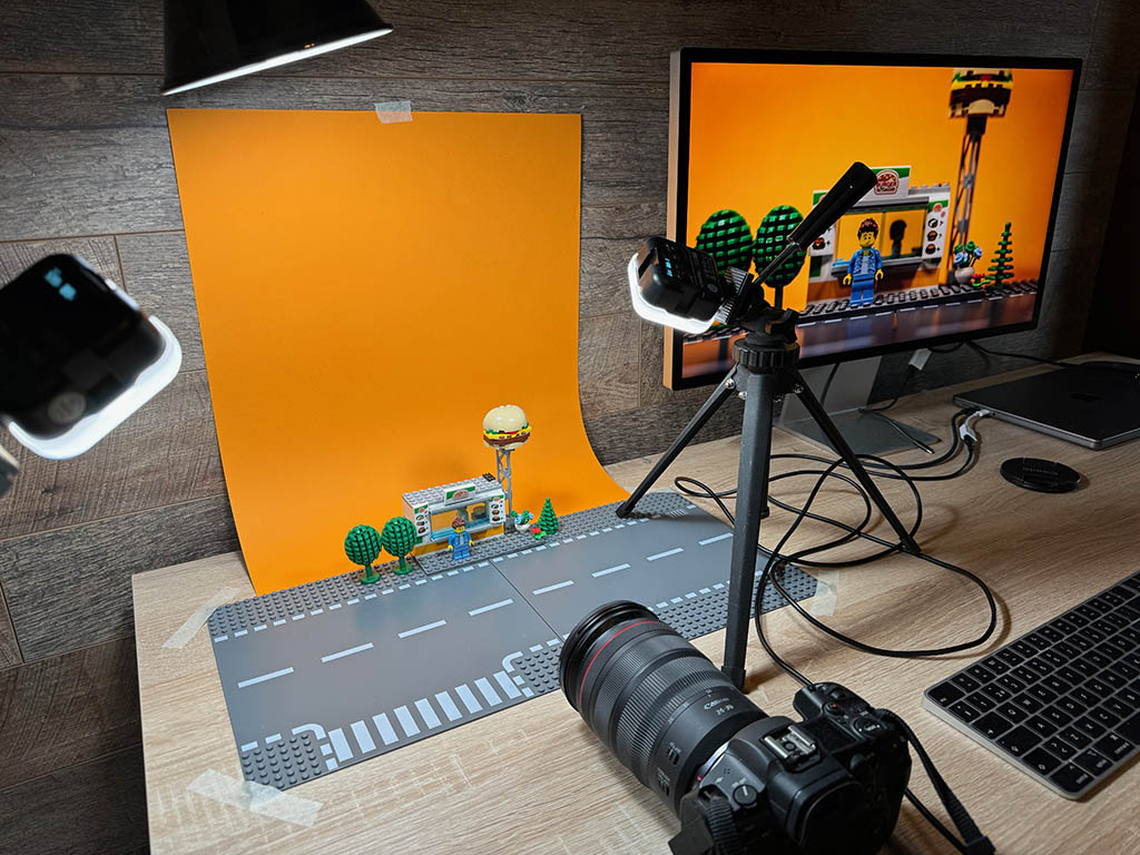 Apple Studio Display ja Canon järjestelmäkamera. Pöydällä myös legoja joita kuvataan ja katsellaan näytöstä.