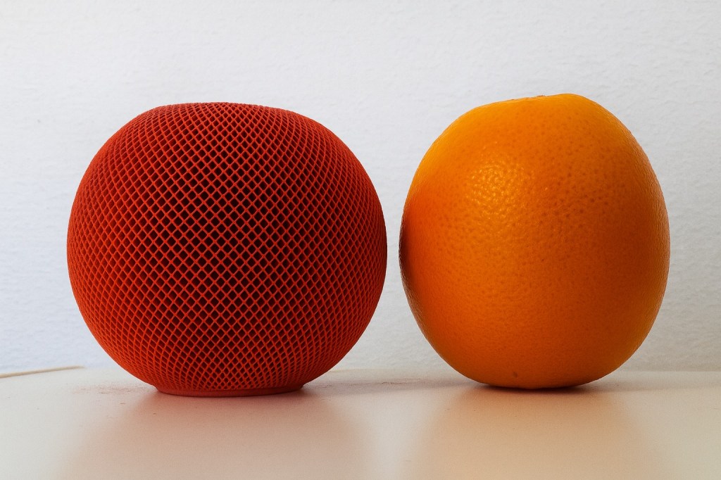 Applen oranssi HomePod mini ja oikea appelsiini vierekkäin. Ne ovat kutakuinkin saman kokoisia keskenään.