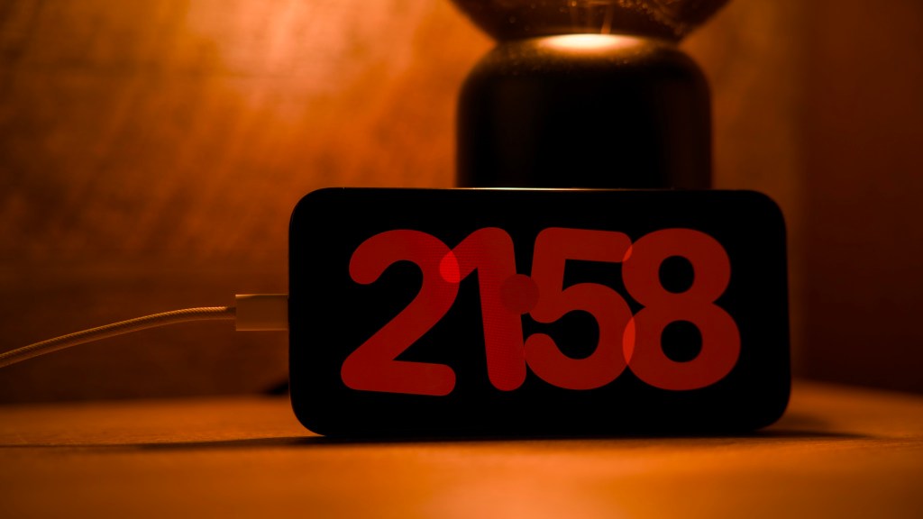 iPhone vaakatasossa latausjohto kytkettynä. Stand-by-tila näkyvissä punaisella näytöllä. Kello on 21.58.