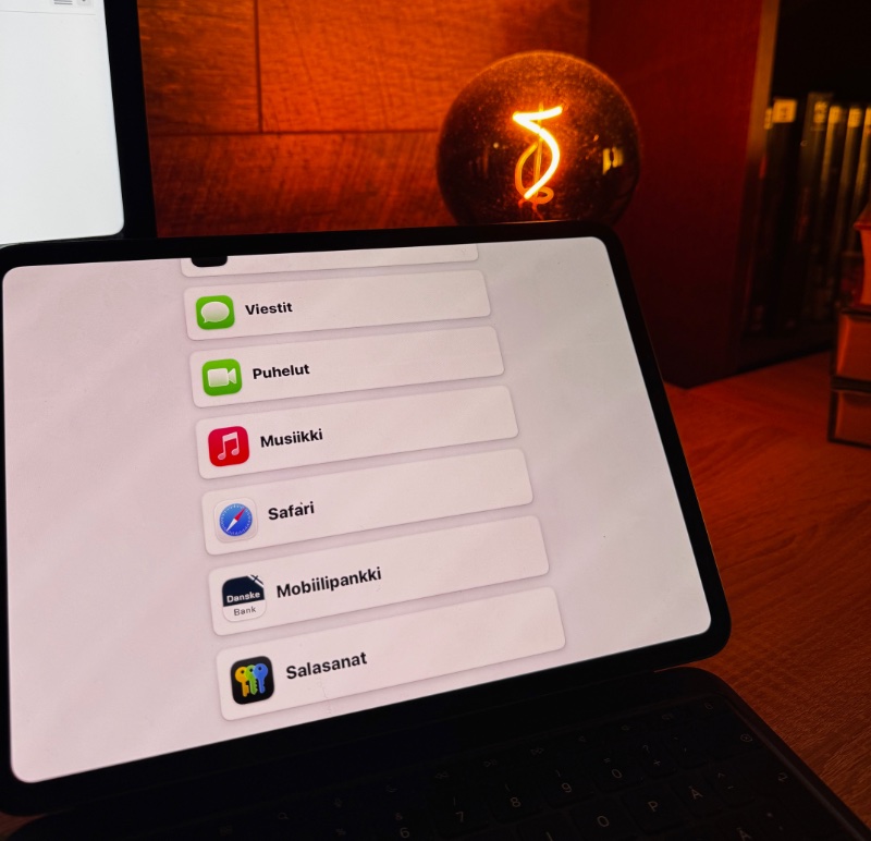 iPadin Avustetun käytön kuvakkeet rivitettynä. Taustalla työpöytä, jolla koristeellinen hehkulamppu. Kuva oranssin sävyinen.
