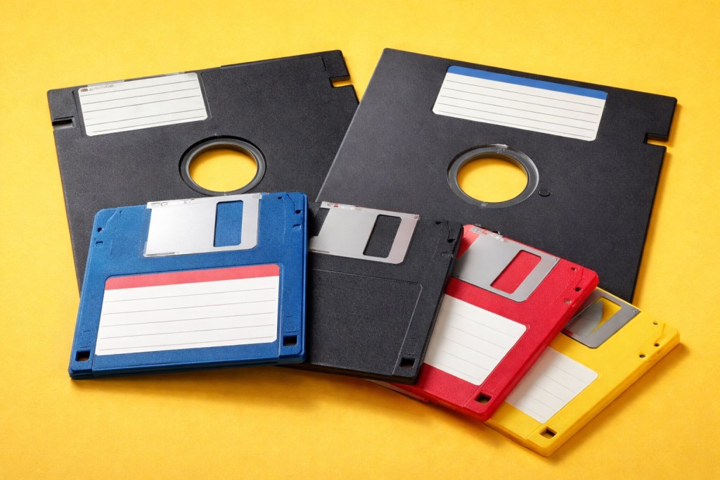 Keltaisella taustalla 3,5" sekä 5,25" levykkeitä.